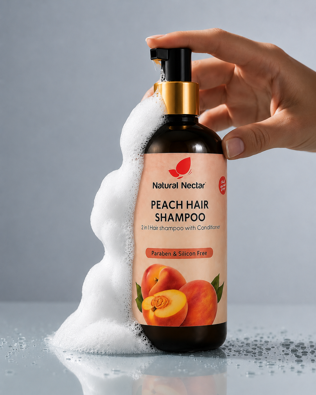 A hand holds a pump bottle of Natural Nectar Peach Hair Shampoo, with white foam dripping from the nozzle onto a gray surface. The bottle has a peach-colored label with an illustration of peaches and a gold collar around the pump.
