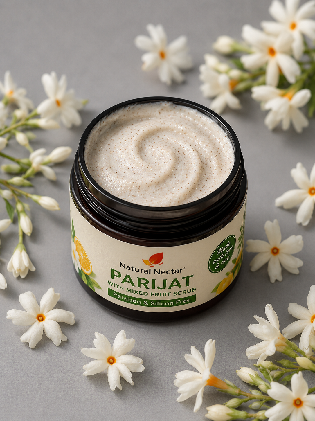 An open jar of Natural Nectar Parijat Mixed Fruits Scrub with cream-colored scrub visible inside, surrounded by small white flowers on a gray surface.