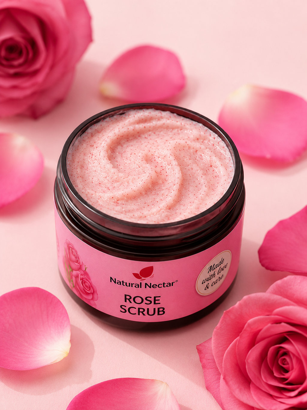 A jar of Natural Nectar Rose Scrub with pink whipped scrub visible inside, surrounded by pink rose petals and roses on a soft pink background.