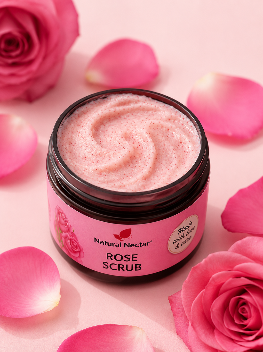 A jar of Natural Nectar Rose Scrub with pink whipped scrub visible inside, surrounded by pink rose petals and roses on a soft pink background.