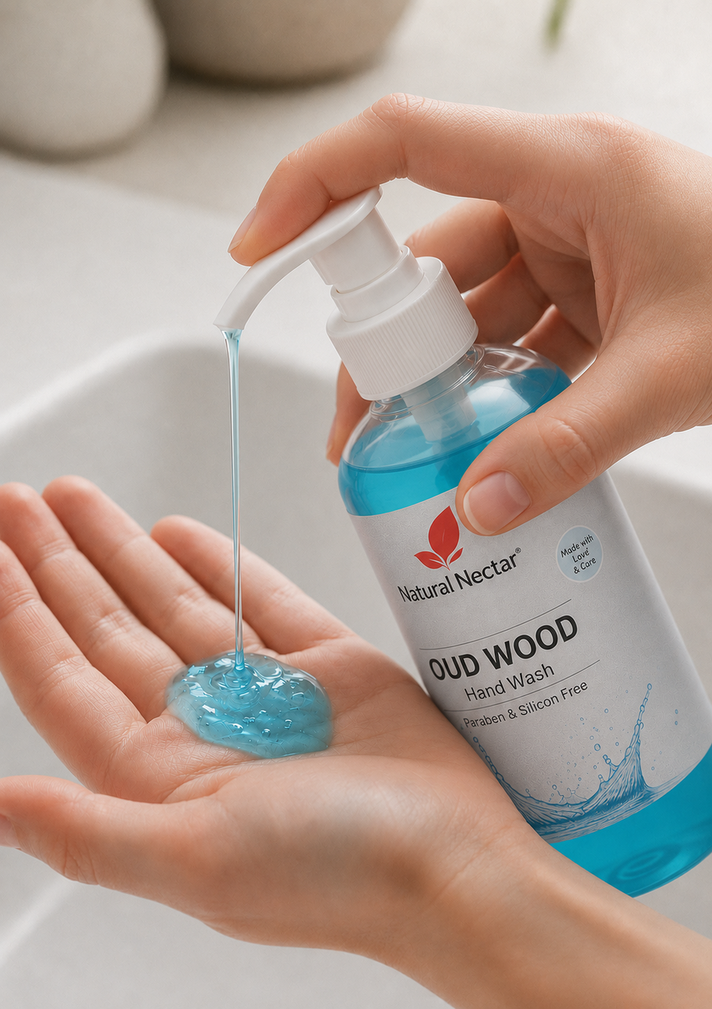 A close-up of a hand dispensing blue hand wash from a Natural Nectar bottle into another hand, with a white sink and soft neutral background.