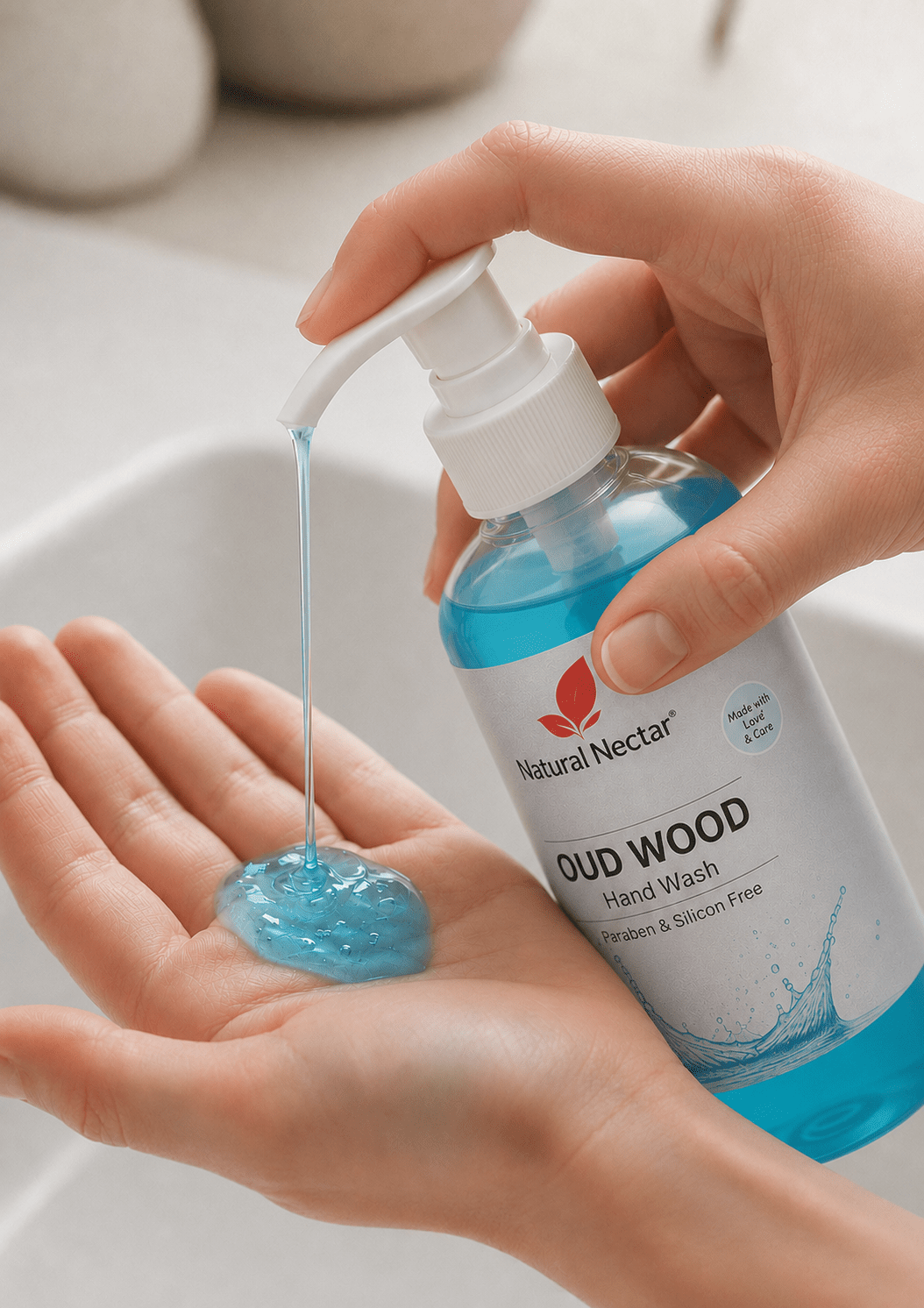 Close-up of a hand dispensing blue Oud Wood hand wash from a Natural Nectar pump bottle into another hand, with white sink background.