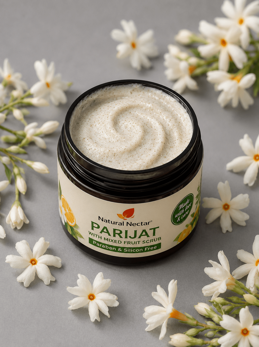An open jar of Natural Nectar Parijat Mixed Fruit Scrub showing the cream-colored scrub texture, surrounded by white flowers.