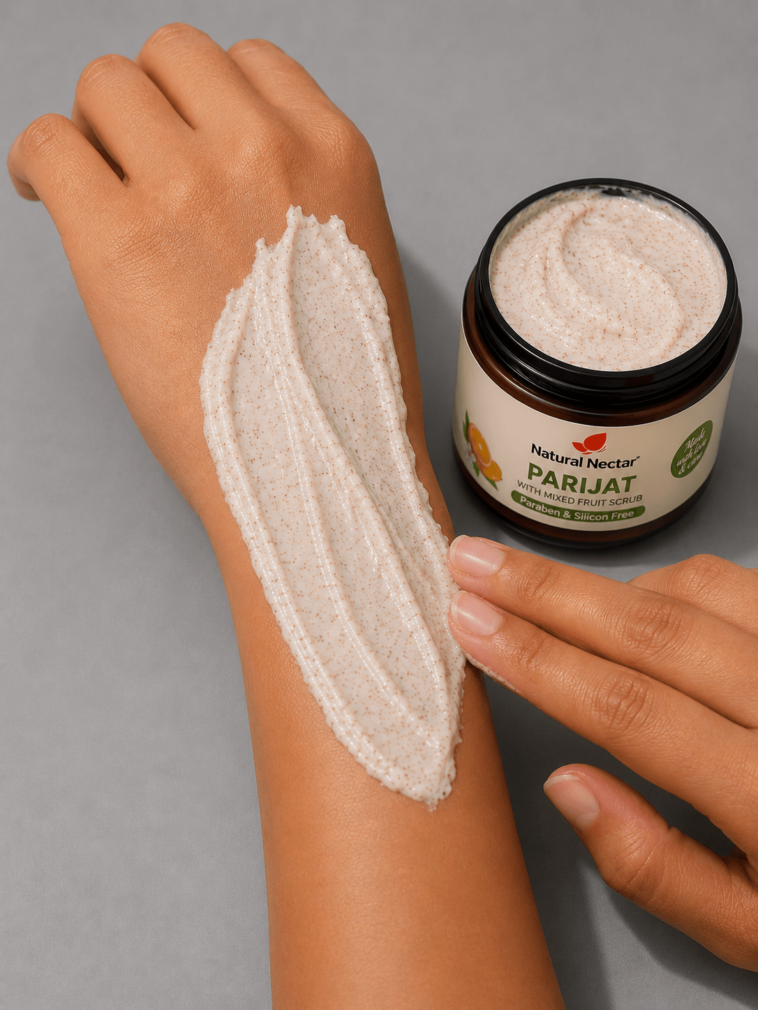 Close-up of exfoliating scrub applied to a person's forearm in a long streak on grey background.