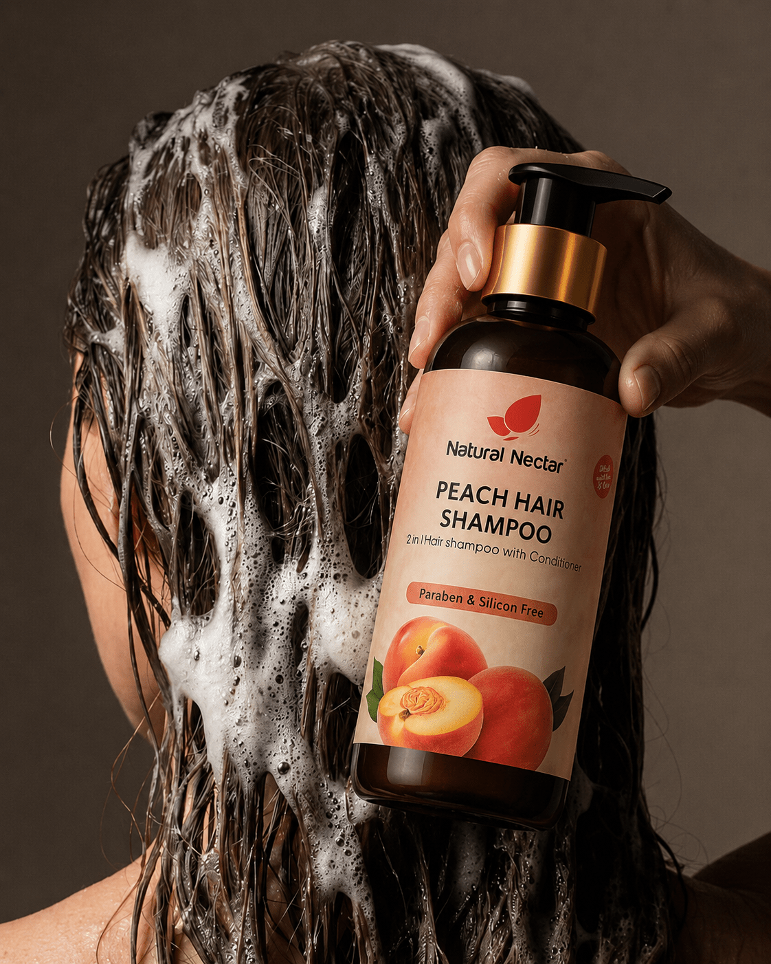 A hand demonstrates Natural Nectar Peach Shampoo applied to dark, wet foamy hair against a blurred background.